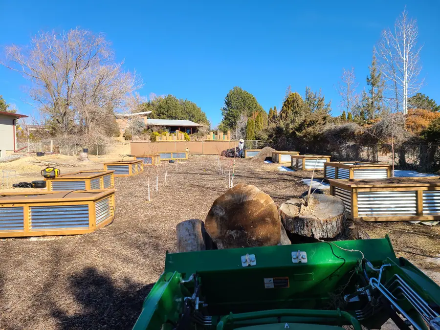 The new raised beds, wooden frames with corrugated metal sides, seen over a tractor bucket holding cut log rounds.